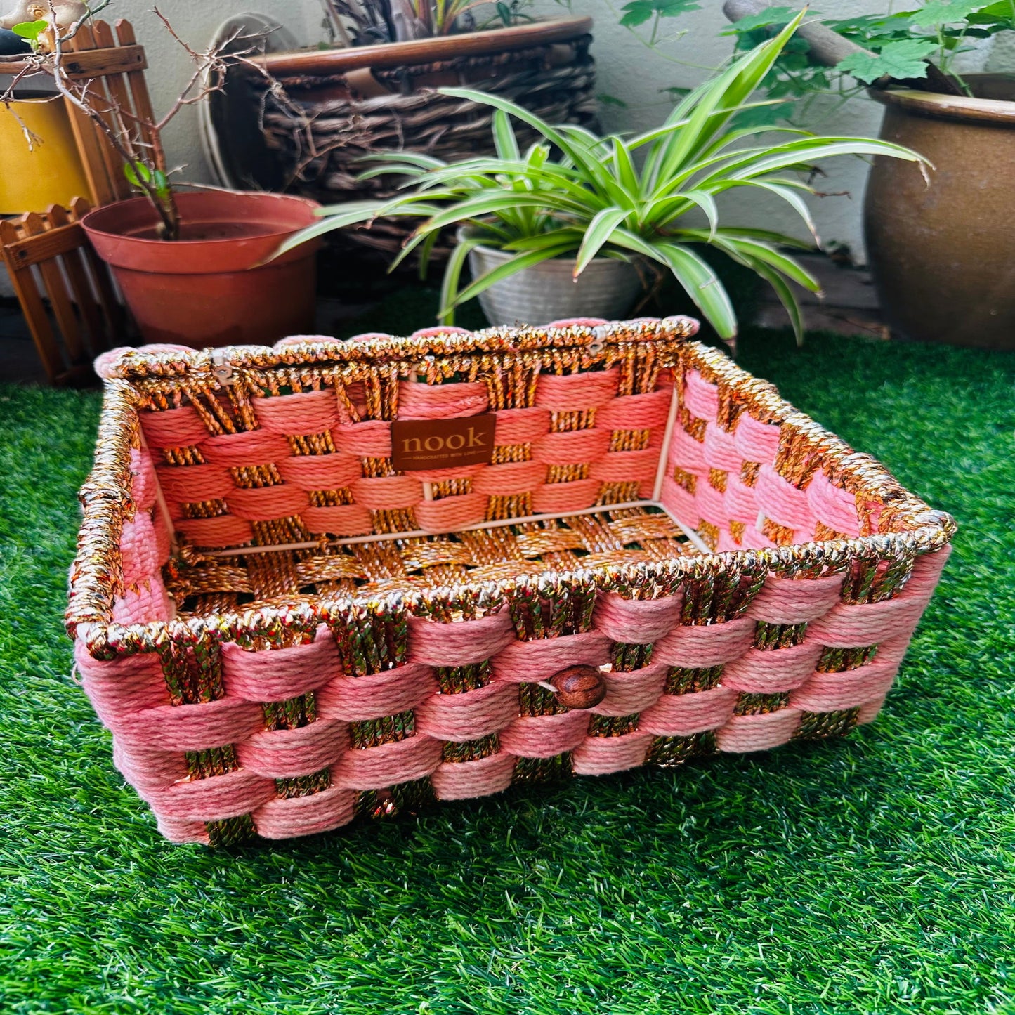 Woven basket with pink and gold pattern on a grassy surface