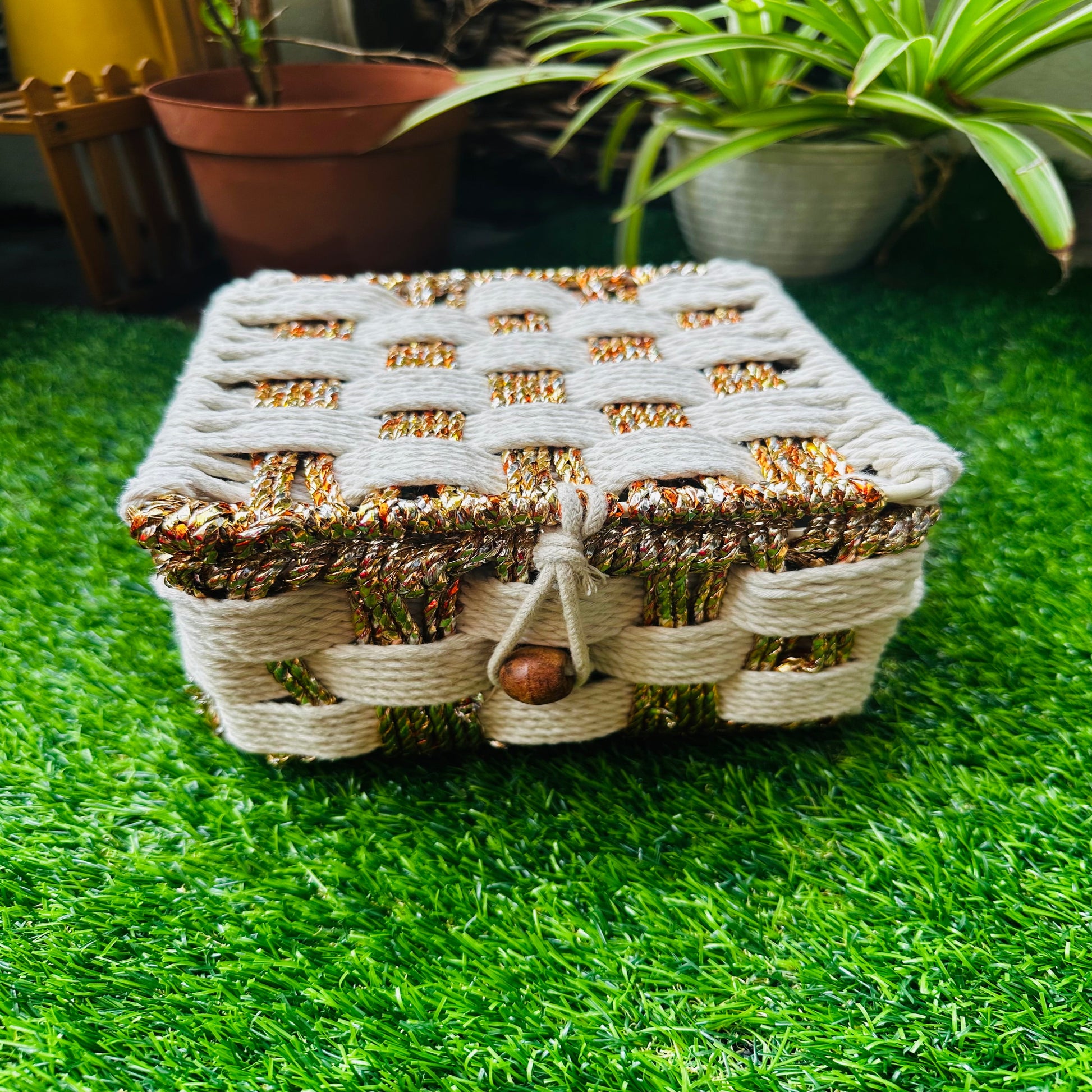 Woven decorative box on a green grass-like surface with plants in the background
